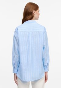 Light blue shirt featuring vertical white stripes, long sleeves, buttoned cuffs, and a back yoke detail, made from a lightweight fabric.