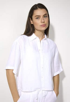 Chemise en lin blanc à manches courtes, devant boutonné, coupe légèrement ample et ourlet arrondi. Présente un col pliable et une texture subtile.
