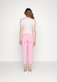 Top de manga corta en rosa claro con textura suave, combinado con pantalones cortos estampados en rosa y zapatos blancos sin cordones, visto desde atrás.