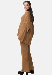Breikset in kamelkleur, met een oversized top met wijde mouwen en bijpassende aansluitende broeken met ribbelstructuur. Dikke zwarte platform schoenen.
