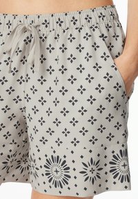 Shorts gris clair avec une taille à cordon, ornés d'un motif floral noir et géométrique, et dotés de poches latérales. Tissu doux avec une texture lisse.