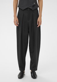 Prispôsobené tmavosivé nohavice s záhybmi, vysokým pásom a voľným strihom. Doplnené o čierne nazúvacie topánky a priliehavú vestu.