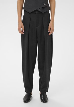 Prispôsobené tmavosivé nohavice s záhybmi, vysokým pásom a voľným strihom. Doplnené o čierne nazúvacie topánky a priliehavú vestu.