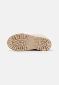 Suela de zapato beige con una superficie de goma texturizada, que presenta un patrón en zigzag, un logo y marcas de tamaño. Diseño duradero para proporcionar tracción.