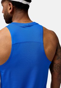 Blå idrottstopp i tanktop-stil med nättextur, breda axelband och rundad halsringning. Har minimala sömmar och en slät tygfinish.