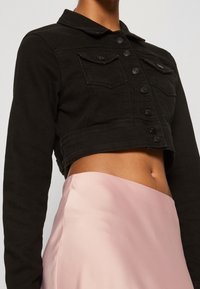 Person wearing a black cropped denim jacket with front buttons and chest pockets, paired with a high-waisted pale pink satin skirt.