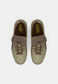 Sneakers Puma KING w oliwkowym i brązowym kolorze. Posiadają miękką teksturowaną cholewkę, wyściełany język oraz kontrastowe sznurowadła. Widoczne akcenty złotego logo.