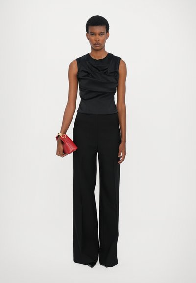 Black sleeveless top with draped detailing, paired with high-waisted black wide-leg trousers. Model holds a small red handbag.