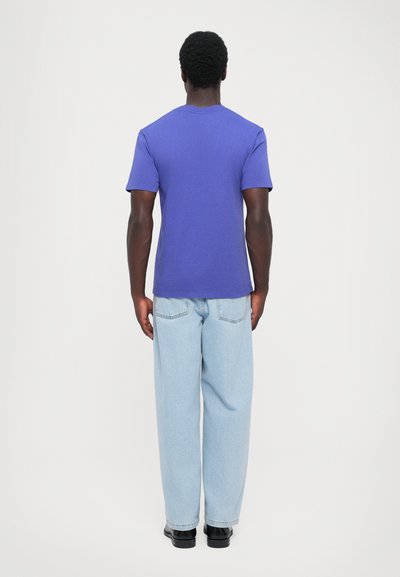 Purple short-sleeve t-shirt made of smooth fabric, featuring a crew neckline. Paired with light blue loose-fit jeans and black shoes.