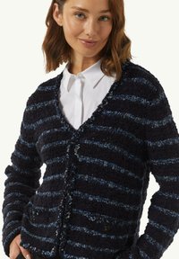 Strick-Cardigan in Marineblau mit blauen Streifen, V-Ausschnitt, strukturiertem Stoff und zwei Fronttaschen mit schwarzen Knöpfen.