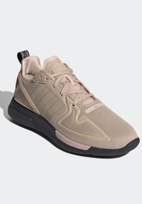 Beige athletic shoe with a mesh upper, pink accents, three side stripes, a textured sole, and a black rubber outsole.