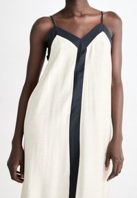 Krämm färgad och svart ärmlös klänning med V-ringning, prydd med ett vertikalt svart rand ner längs framsidan och en lätt tygtextur.