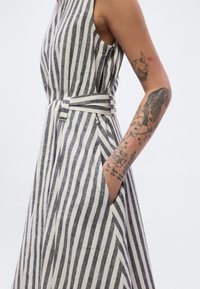 Ριγέ φόρεμα από βαμβάκι σε γκρι και λευκό, με εφαρμοστή μέση και ζώνη που δένει, πλαϊνές τσέπες και αμάνικη σχεδίαση.