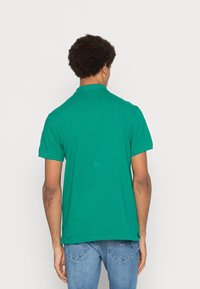 Zielona bawełniana koszulka polo z klasycznym kołnierzykiem i krótkimi rękawami. Posiada prosty dół i subtelne boczne rozcięcia dla swobody ruchów.