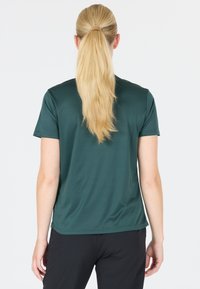 Kortärmad grön sporttröja med en slät och andningsbar textur. Har en avslappnad passform som hänger något över ryggen och axlarna.