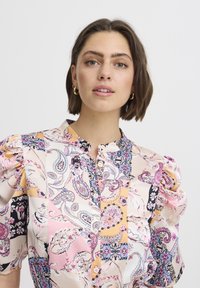 Bluză multicolor cu mâneci voluminoase, guler mandarin și închidere cu nasturi. Fabricată dintr-un material neted cu modele paisley și florale.