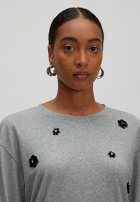 Grijze oversized sweatshirt met zwarte bloemenversieringen, ronde halslijn en korte mouwen, gemaakt van een zachte, textuurstof.