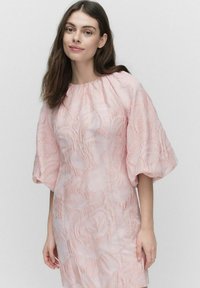 Vaaleanpunainen kukallinen teksturoitu mekko, jossa on lyhyet puffihihat ja pyöreä pääntie. Kangas sisältää hienovaraisen kohotetun kuvion koko alueella.