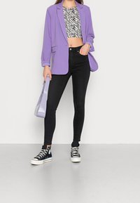 Blazer de lavanda, top negro corto de estampado de cebra, jeans ajustados negros y zapatillas altas negras. Los accesorios incluyen un bolso ligero de color púrpura.