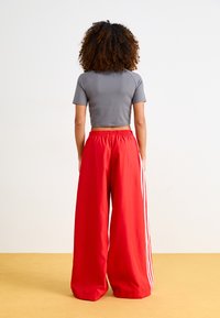 Pantalons larges rouges avec une taille élastique et des rayures blanches sur les côtés ; associés à un haut court gris ajusté. Texture du tissu lisse.