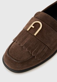 Brūni zamša loafers ar fringu un zelta toņa metāla akcentu augšpusē. Melna zole un gluda tekstūra.