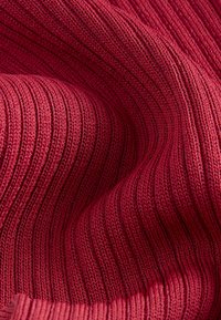 Gros plan sur un tissu tricoté côtelé rouge avec une texture visible et des plis créant des lignes courbes.