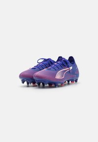 Purple and pink soccer cleats with a textured mesh upper, lace-up design, and rubber studs on a blue outsole. Notable logo accent on side.