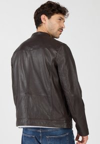 Braune Lederjacke mit strukturiertem Design, mit hohem Kragen, Nähdetails und glatter Textur. Sichtbare Taschen und taillierte Passform.