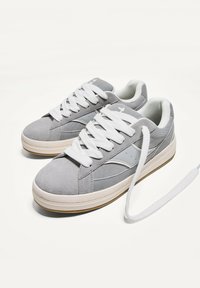 Sneakers in suede grigio con lacci bianchi, caratterizzati da un corpo testurizzato, accenti laterali lisci e una suola in gomma. Design classico con punta arrotondata.