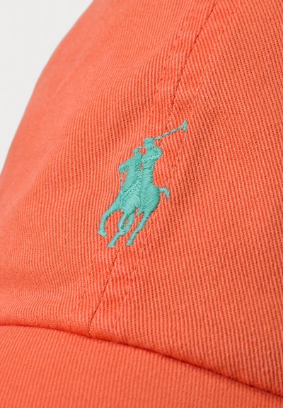 Oranža cepure, izstrādāta no teksturētas auduma, ar izteiktu tirkīza izšuvumu polo spēlētāja logotipu priekšā.