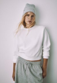 Biely krátky mikina s rebrovanými man�žetami a ramenami, doplnená sivými teplákmi so sťahovacou šnúrkou. Mäkká textúra, ležérny dizajn.