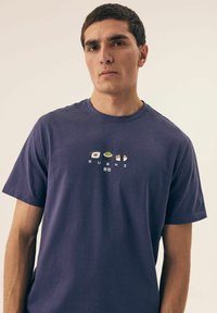 Purple cotton t-shirt featuring a graphic design of sushi rolls and the word "SUSHI" in English and Japanese, crew neckline, short sleeves.