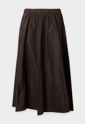 Femme portant un haut rose à manches courtes, un pantalon noir taille haute à jambes larges et des ballerines noires, debout avec une main dans la poche.