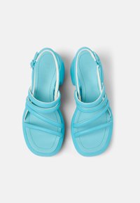 Sandales en cuir bleu avec plusieurs sangles croisées, bout rond et un talon bas et épais. Fini lisse avec des accents blancs contrastés.