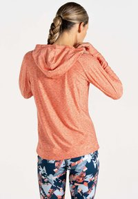 Korallefarbener, kapuzenloser Sportpulli aus strukturiertem Material, kombiniert mit Leggings mit buntem Muster in Blau, Orange und grauen geometrischen Designs.