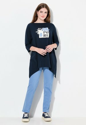 T-shirt blu navy con un design grafico floreale che presenta la parola "PURE." Abbinato a pantaloni azzurri e sneakers blu navy.