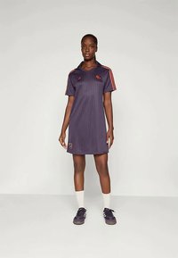 Jūras spēku svītrainā sporta kleita ar apkakles izgriezumu, sarkaniem akcentiem, īsām piedurknēm un logotipu uz krūšu un apakšmalas, kombinēta ar melniem sporta apaviem.