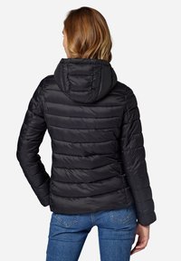 Černá bunda typu puffer s přiléhavou kapucí, horizontálně prošívaným designem a dlouhými rukávy, spárovaná s modrými džínami. Hladký povrch a lesklý vzhled.