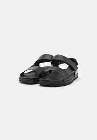 Black leather sandals featuring cross straps and a back support. Cushioned footbed and textured rubber sole for grip.