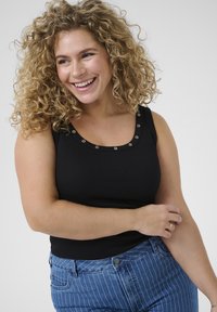 Musta ribbattu tank top, jossa on pyöreä pääntie ja metalliset reikäkohokohdat, yhdistettynä sinisiin raidallisiin korkeavyötäröisiin farkkuihin.