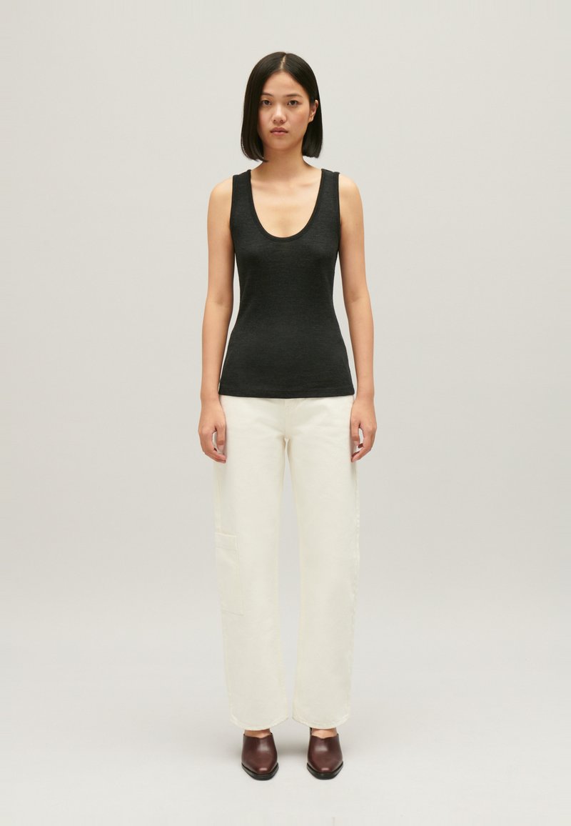 Zwart mouwloos topje met een ronde halslijn, gedragen met crèmekleurige wijde broek en bruine hoge hakken, weergegeven tegen een neutrale achtergrond.