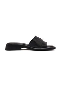 Sandale slide en cuir noir avec un petit talon bloc et de larges brides croisées sur le pied, présentée de côté sur fond blanc.