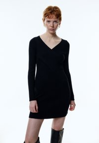 Schwarzes, langärmliges Strickkleid mit V-Ausschnitt und geometrischem Muster im Bereich des Rumpfes. Strukturiertes Material mit figurbetonender Silhouette.