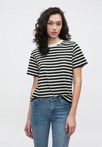 Schwarz-weiß gestreiftes T-Shirt mit rundem Ausschnitt und kurzen Ärmeln, kombiniert mit blauen Jeans.