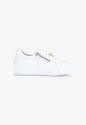 Witte platformsneaker met geribbelde zool, gouden rits aan de zijkant en decoratieve gouden hanger aan witte veters, weergegeven in zijaanzicht.