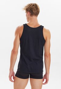 Sort bomulds tanktop med rund halsudskæring, ærmeløst design og tætsiddende pasform. Udsigten er fra ryggen, som viser muskuløse skuldre og arme.