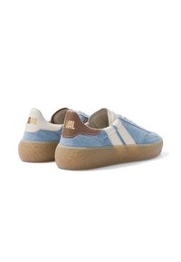 Paire de baskets en daim bleu avec des bandes blanches, des languettes de talon crème et marron, et des semelles en caoutchouc beige épaisses et texturées, vues de dos et de côté.