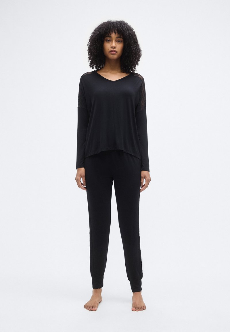 Ensemble de vêtements de détente noirs comprenant un haut à manches longues avec un col en V et une coupe légèrement courte, associé à un pantalon assorti avec une taille élastique.