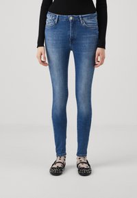 Jeans ajustados de color azul con un lavado desgastado, diseño de cinco bolsillos, cierre frontal con botón y ligera elasticidad, combinados con unos zapatos planos negros y calcetines con estampado.