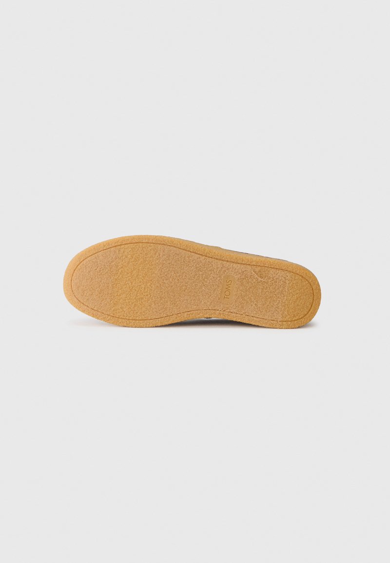 Zapato con una suela de goma marrón que presenta una superficie texturizada y un logotipo sutil. El diseño es funcional con una forma curva.